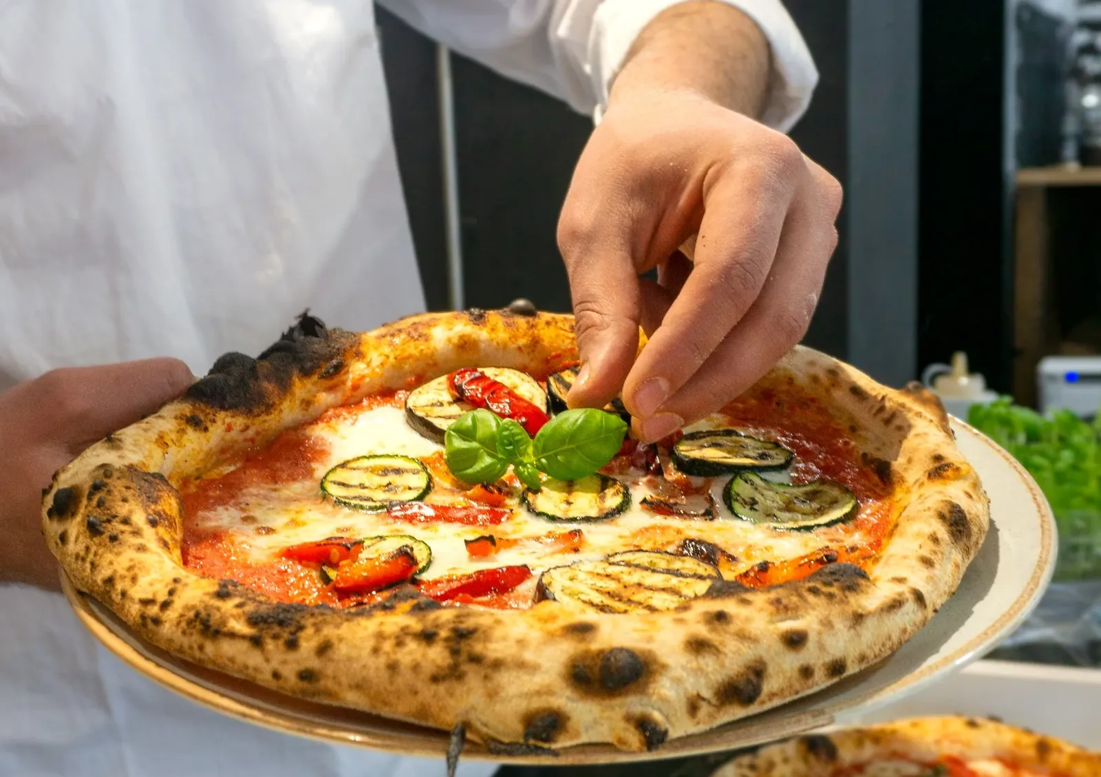 Ein Pizzaiolo legt frisches Basilikum auf eine Pizza mit Lachs, Zitrone und Mozzarella.